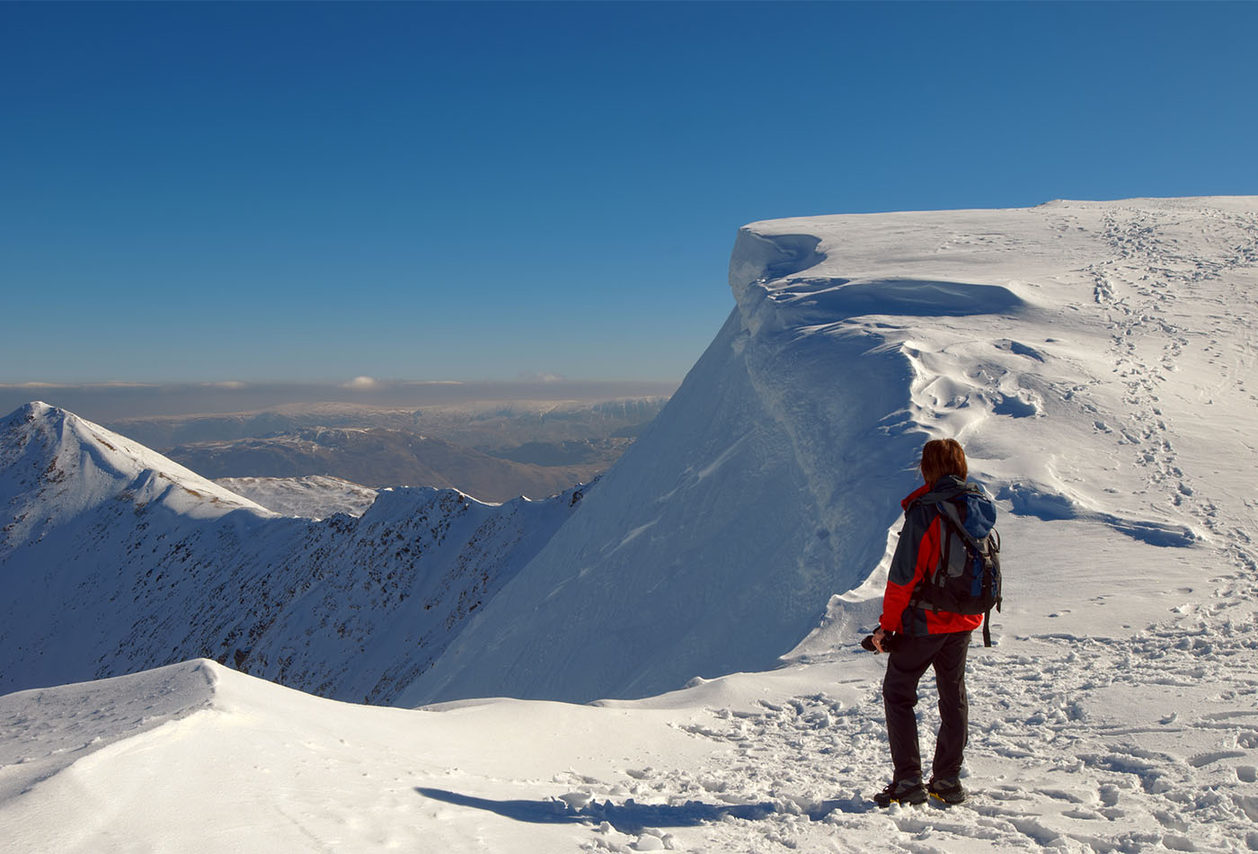 Rear view of female mountaineer on snowy summit of Helvellyn mountains in Winter, Lake District National Park, Cumbria, England. Winter hiking