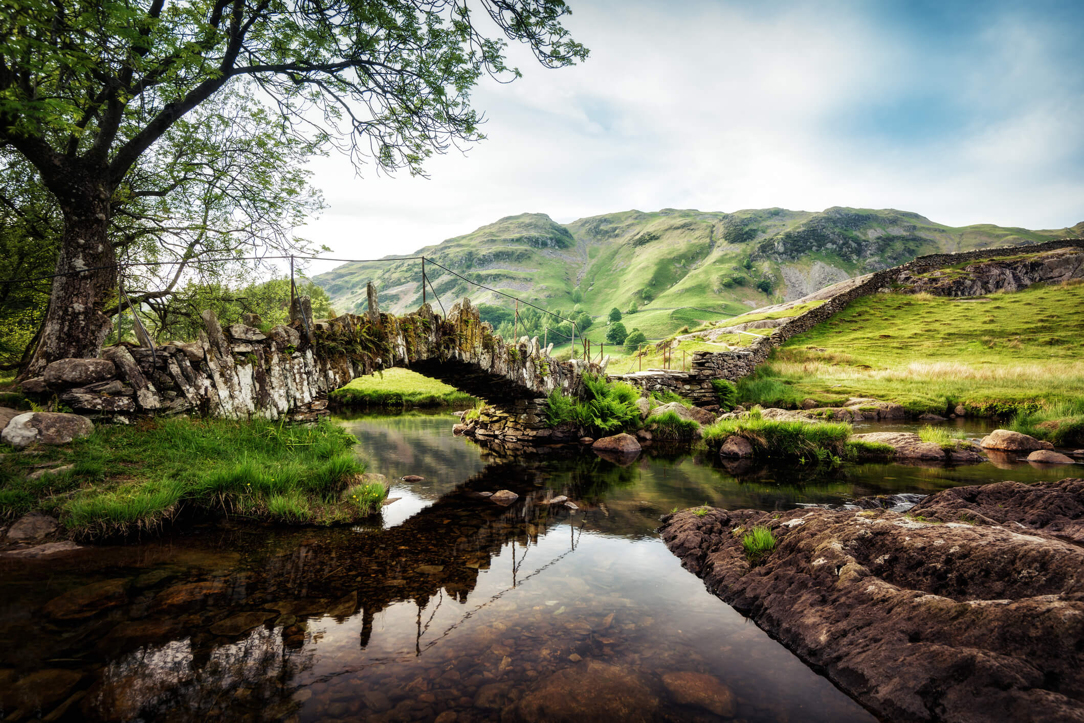 Slaters Bridge Lake District United Kingdom - traditional stone bridge over a river with green mountains in the background