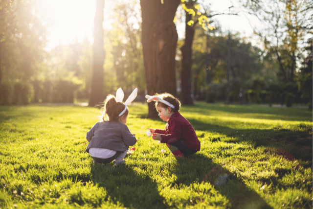 Two children playing a field with easter bunny ears on.