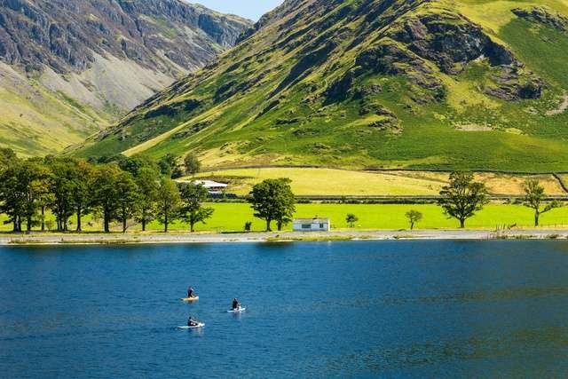 Buttermere lake with a mountain range backdrop and people paddleboarding.