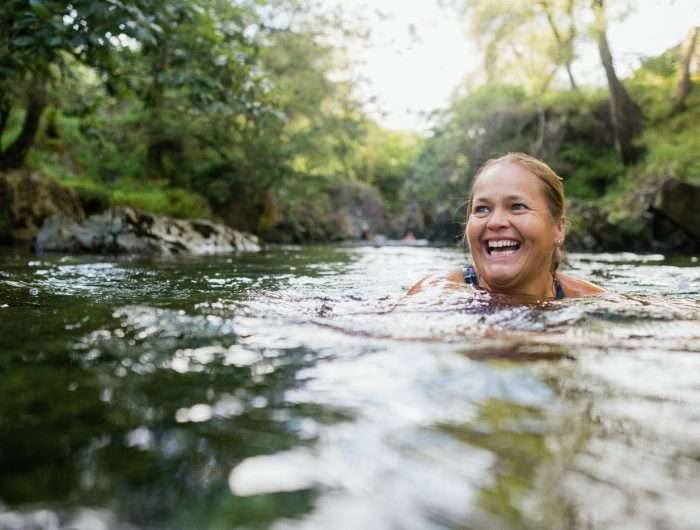 A person smiling and wild swimming in a lake.