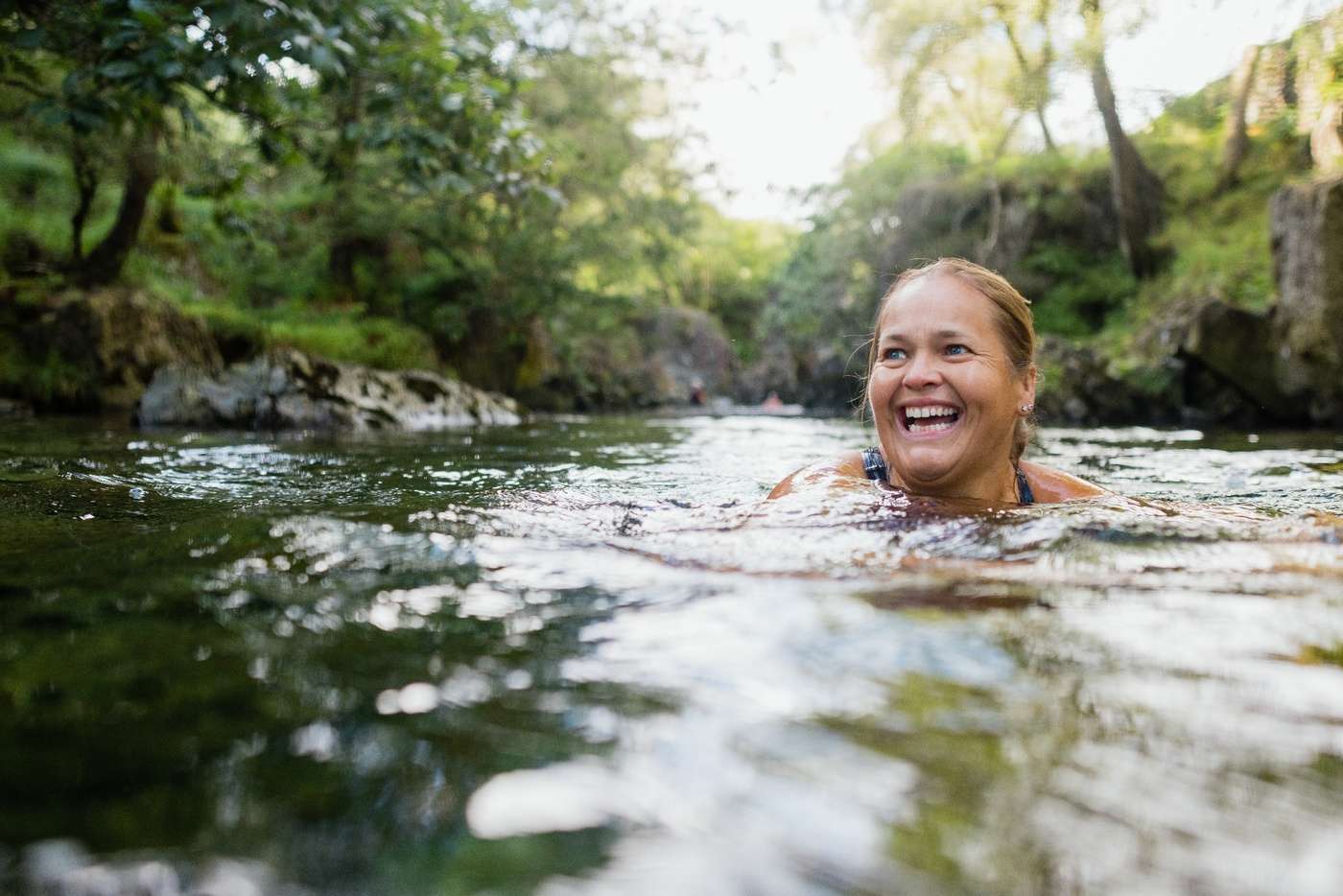 A person smiling and wild swimming in a lake.
